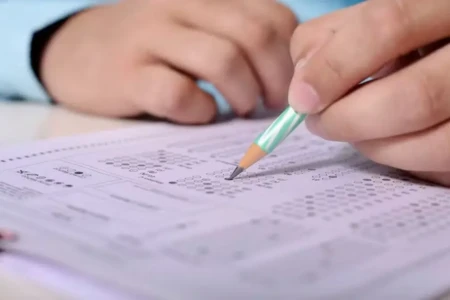 Pessoa preenchendo prova de concurso público em mesa de estudos