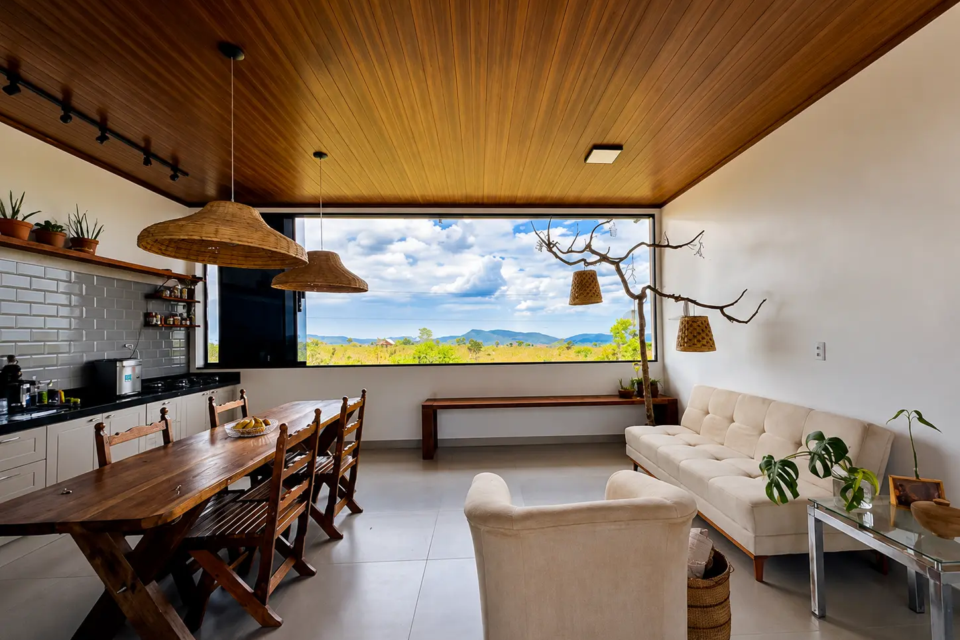 Ambiente interno de hospedagem anunciada no Airbnb em Goiás combina madeira, grandes aberturas e integração com a paisagem do Cerrado, em proposta que transforma a própria estadia em parte da experiência turística. (Foto: Reprodução/Airbnb)