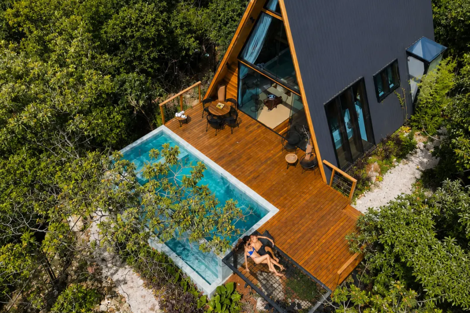 Cabana em formato A-frame, cercada pelo Cerrado, combina grandes áreas de vidro, deck de madeira e piscina privativa, em uma das hospedagens selecionadas pelo Mais Goiás pela arquitetura e integração com a paisagem. (Foto: Reprodução/Airbnb)
