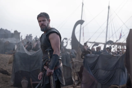 Matt Damon como Odisseu em cena de “A Odisseia”, diante de navios e tendas de um acampamento